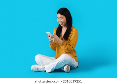 Entertainment and gadgets. Cheerful smiling attractive young asian woman using smartphone on blue studio background, checking newest mobile app, shopping, banking, studying online, copy space - Powered by Shutterstock