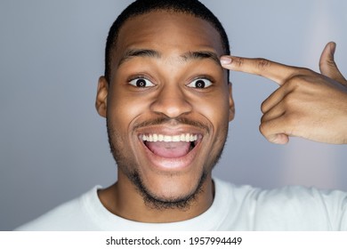 Enthusiastic African Man. Aha Moment. Self Motivation. Portrait Of Happy Astonished Handsome Dark Skin Guy In White Pointing At Face Temple Smiling Isolated On Gray Background.