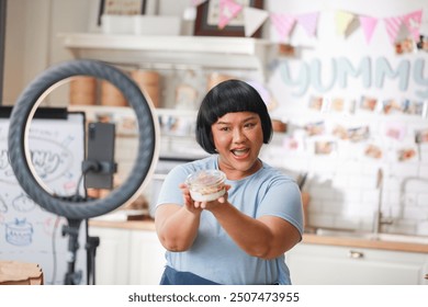 Enthusiastic Asian Content Creator Presenting Food Item in Modern Kitchen Setup, including ring light and smartphone, to film culinary tutorial or review. Small Business Concept - Powered by Shutterstock