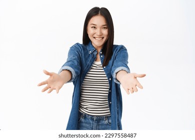 Enthusiastic asian girl extends her hands forward in welcome gesture, receive smth, reaching for hug, smiling while standing over white background. - Powered by Shutterstock