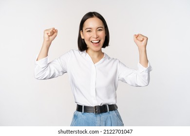 Enthusiastic asian woman rejoicing, say yes, looking happy and celebrating victory, champion dance, fist pump gesture, standing over white background - Powered by Shutterstock