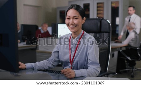 Enthusiastic beginner young asian it programmer working on desktop computer. Female specialist creating innovative software looking at camera and smiling