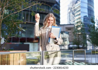 Enthusiastic businesswoman feels upbeat after morning cup of coffee, raise her cup up and dances outside. - Shutterstock ID 2230814233
