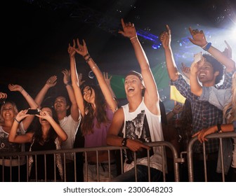 Enthusiastic crowd with arms raised behind railing at concert - Shutterstock ID 2300648203