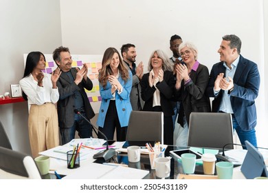 Enthusiastic diverse business team applauding a successful presentation. Multigenerational professionals in modern office with sticky notes and messy desk. Workplace diversity and project achievement. - Powered by Shutterstock