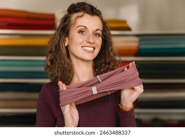 Enthusiastic fashion designer proudly displaying a freshly made textile accessory in her well-organized studio, surrounded by colorful fabric rolls - Powered by Shutterstock