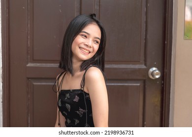 An Enthusiastic Female Teenager Glances Sideways And Smiles As She Looks At Her Pets Playing Outside The House.