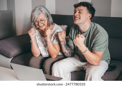 Enthusiastic generations  family fans watching football championship or olympic games on laptop sitting together on sofa, happy grandson with his grandmother celebrate team victory - Powered by Shutterstock