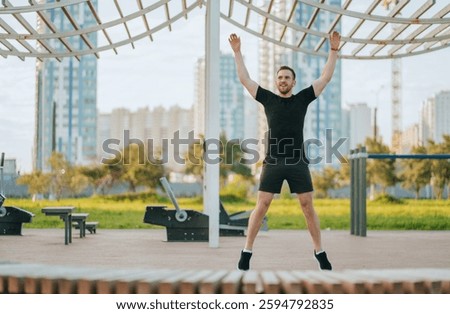 Enthusiastic and lively, a man performs jumping jacks under a modern open structure with a city backdrop.
