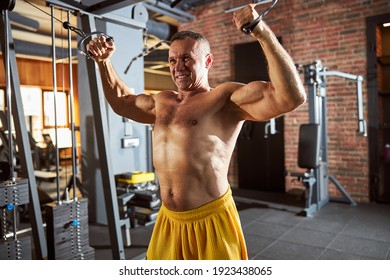 Enthusiastic man with no shirt on doing arm exercises wiht weights at the well-furnished gym