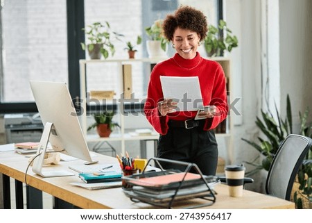An enthusiastic manager reviews documents while standing at her desk in a contemporary workspace.