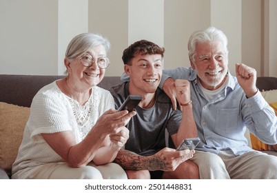 Enthusiastic multigenerational family fans watching sport games on TV sitting together on sofa, happy grandparents and young grandson expressing hope of winning - Powered by Shutterstock