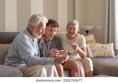 Enthusiastic multigenerational family fans watching sport games on smartphone sitting together on sofa, happy grandparents and young grandson expressing joy - Powered by Shutterstock