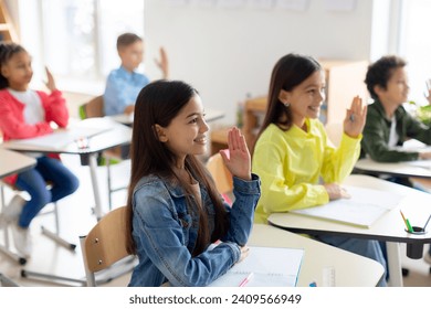 Enthusiastic school children, sitting attentively at desks in classroom, eagerly raising their hands to actively participate in learning experiences - Powered by Shutterstock