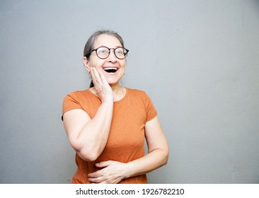 Enthusiastic and surprised elderly woman in  brown T-shirt on  gray background