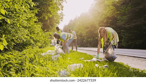 Enthusiastic team of caring volunteers cleaning up area near road. Beautiful young Caucasian woman and group of multicultural people picking up trash and putting it in garbage bags. Pollution concept. - Powered by Shutterstock