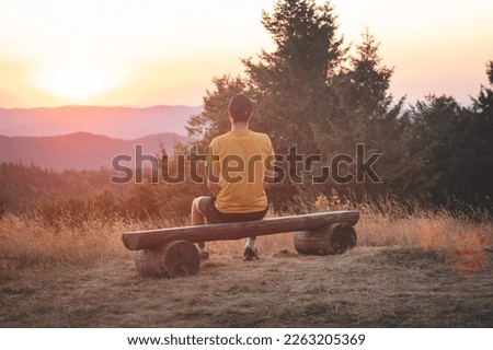 Enthusiastic traveler sits on a wooden bench and watches the last remnants of sunshine in the raw nature. Sunset on Horni Becva, Beskydy mountains, Czech republic.