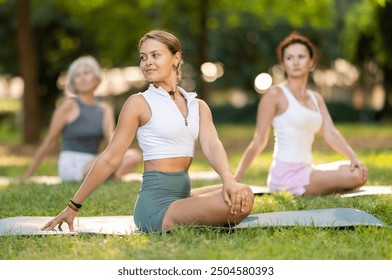 Enthusiastic young female yoga instructor leading outdoor group class in tranquil setting amidst lush greenery of city park, performing stretching exercises in Padmasana pose.. - Powered by Shutterstock