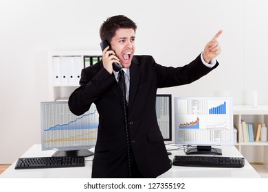 Enthusiastic Young Male Stock Broker In A Bull Market Holding A Telephone And Yelling Out A Buy Or Sell Order On Stocks Or Bonds