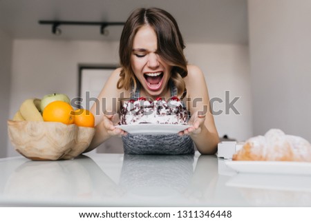 Enthusiastic young woman eating creamy pie. Carefree female model enjoying fruits and cake.