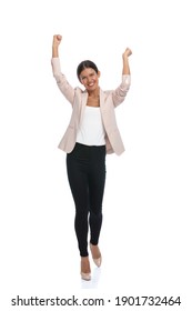 enthusiastic young woman in pink jacket holding arms in the air, laughing and cheering, walking isolated on white background in studio, full body