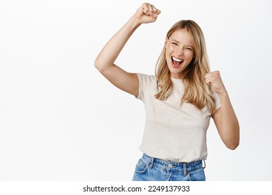 Enthusiastic young woman winning on mobile phone, celebrating and cheering, shouting with joy, standing over white background