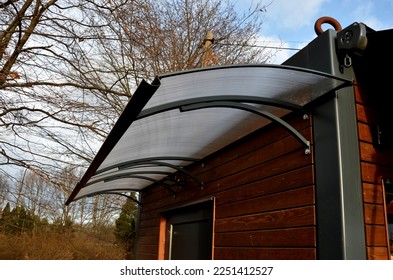 entrance to the building with a polycarbonate roof over the door. plexiglass bent and equipped with a metal gutter. a living container lined with planks and painted with brown glaze.garden office - Shutterstock ID 2251412527