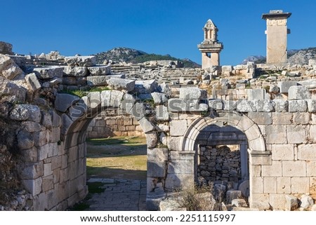 Entrance gate to theatre of Xanthos ancient city - part of Lycian way. Tomb monument of king Kybernis ( Harpy Tomb), Pillar Tomb on background. Popular travel destination in Antalya, Turkey