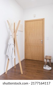 Entrance Hall Area In Modern Apartment. Vertical View Of Hallway With Clothes On Coat Hanger, Small Handcrafted Wood Bench For Shoes And Wooden Door In Entryway