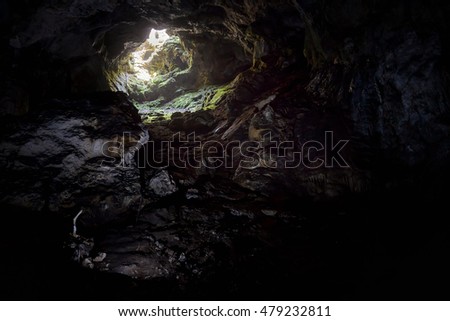 Entrance to the karst cave in a mountain. Natural cave opening. Inside the subterranean cave background with copy space. Dark cave with a bright daylight spot of exit.