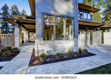 Entrance Of  Luxurious New Construction Home With Blue Siding And Stone Decor. Concrete Walkway Lead To Long Covered Porch With Modern Glossy Front Door. Northwest, USA