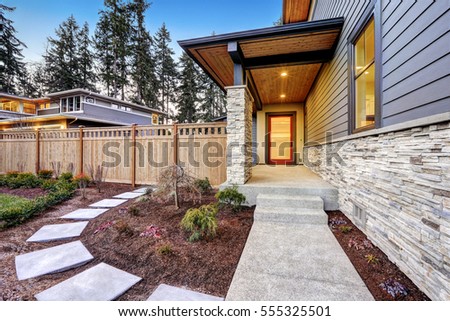 Entrance of  Luxurious new construction home with blue siding and stone decor. Concrete walkway lead to long covered porch with modern glossy front door. Northwest, USA