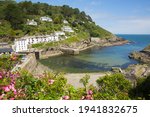 Entrance to Polperro harbour Cornwall UK with clear blue green sea and pink flowers