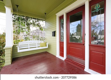 Entrance Porch In Old House With Contrast Green And Red Walls. View Of White Wooden Hanging Swing