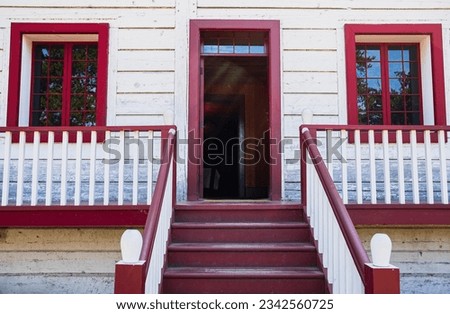 Entrance staircase of a traditional wooden house in North America. White with red railing on white House. Stairs leading up. Detail of a wooden porch - steps and rails