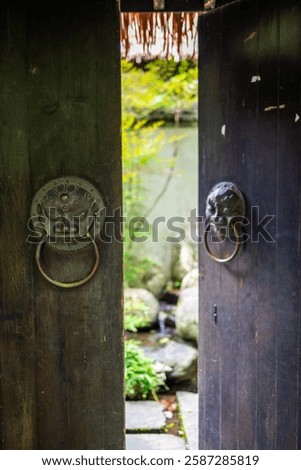 Entrance to a traditional Chinese garden, showcasing a wooden door with intricate metal knockers in the shape of a lion's head.