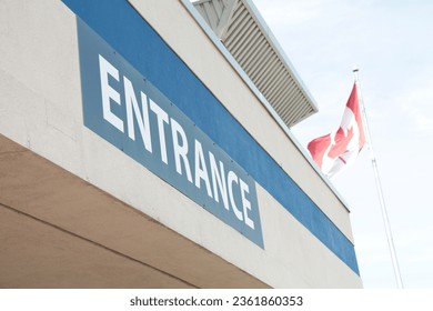 entrance writing caption text facade sign word in white on blue outside exterior outdoors, shot on angle with canada canadian flag blowing behind