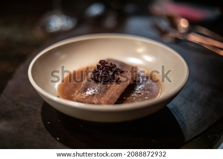 An entree dish of braised fish in rich miso broth on a white serving plate