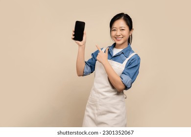 Entrepreneur asian woman wearing aprons and showing blank screen smartphone on light brown background - Powered by Shutterstock