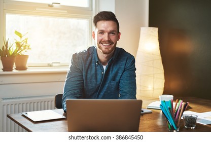 Entrepreneur at office with laptop looking at camera smiling