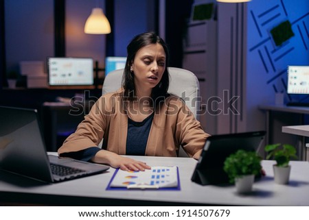 Entrepreneur using tablet pc while working from dark office working on deadline. Business woman working overtime at the office to finish a corporate job using tablet pc.