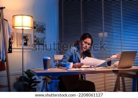 Entrepreneur using tablet pc while working from dark office working on deadline. Business asian woman working overtime at home.