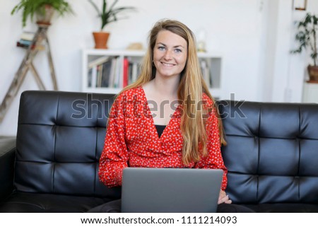 Entrepreneur woman wearing red shirt working with a laptop sitting on a couch at home