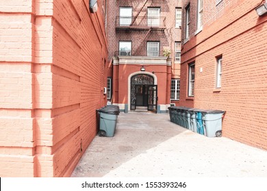 Entry Door Of Orange Brick Old Buildings With Fire Stairs, And Garbage Cans During The Day. Travel And Housing Concepts. Bronx, NYC, USA.