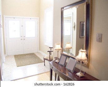 Entry Hall Of A House With White Doors, Windows, Chair, Lamps, Mirror,  Table, Tile Floor And Rug.