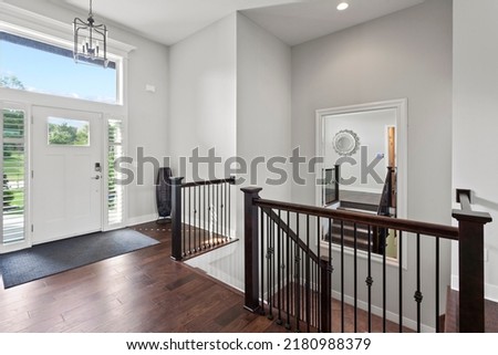 Entry way and staircase with large mirror on wall, hardwood floors and sky lights looking to greenspace