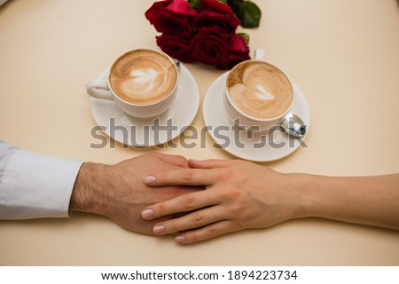 the entwined hands of lovers on the table with coffee mugs