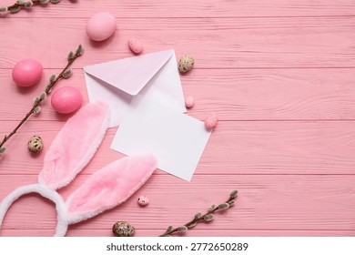 Envelope with blank card, Easter eggs, bunny ears and pussy willow branches on pink wooden background