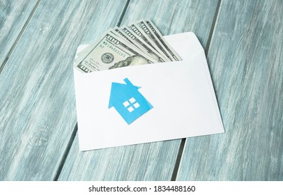 Envelope With Dollars Money And A House On Wooden Background.