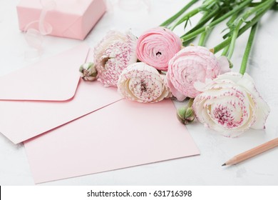 Envelope Or Letter, Paper Card, Gift And Pink Ranunculus Flowers On White Table For Greeting On Mother Or Woman Day. Can Be Used As Wedding Mockup.